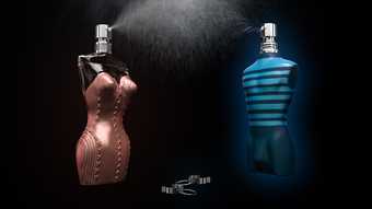 Two perfume bottles on a black background. The female shaped one is spraying perfume at the male one.