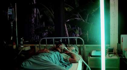 A man lies in a hospital bed with a neon green light beside him