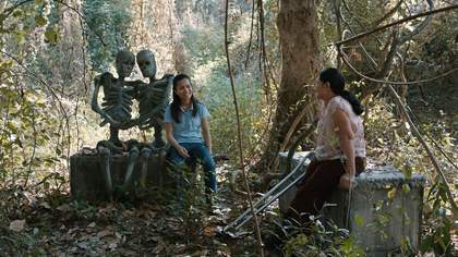 Two people sit in a cemetery with two skeletons 