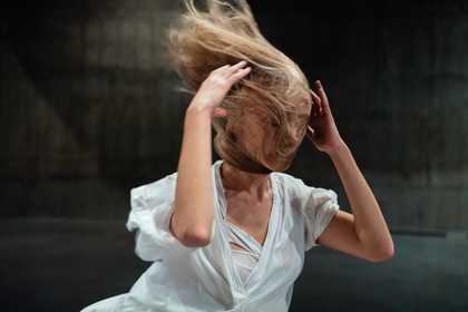 figure with hands either side of their head and long blonde hair blowing across their face.
