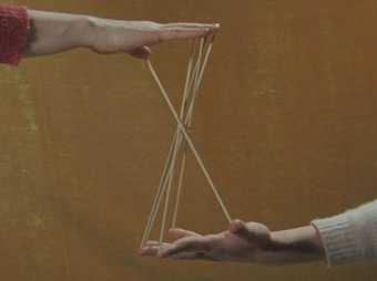 Two hands belonging to different people appear to be playing cats cradle 