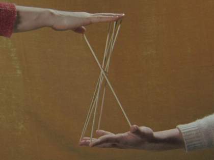 Two hands belonging to different people appear to be playing cats cradle