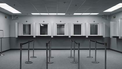 landscape black and white image of an empty queue with booths at the end.