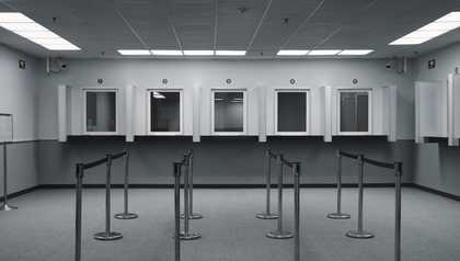 landscape black and white image of an empty queue with booths at the end.