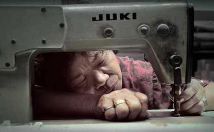 close up of a woman looking into the needle of a sewing machine. her hands are holding the fabric as she inspects the thread.