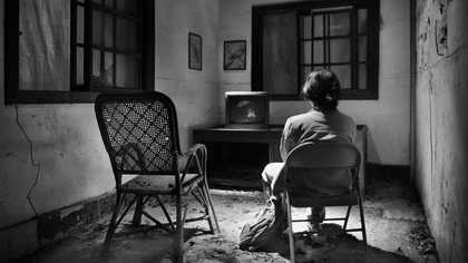 A woman sits on a chair watching her own reflection on a disconnected TV in a room of the abandoned Losheng Sanatorium in Taipei.