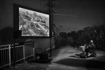 black and white high contrast image of a film being projected onto a screen in a field