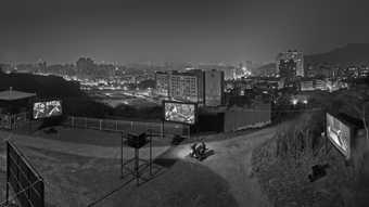 black and white high contrast image of multiple outdoor film screens with a city skyline in the background. there are meandering paths through the screens.