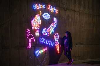 Chila Kumari Singh Burman stands next to a wall in Tate Modern, decorated with her neon light designs