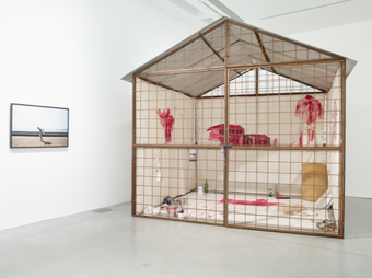 Nikhil Chopra installation in the gallery at Kettle's Yard, a cross section of a single room structure, enclosed by a wire wall, with red murals within