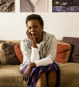 Author Claudia Rankine sitting on a sofa looking into the camera