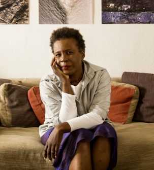 Author Claudia Rankine sitting on a sofa looking into the camera