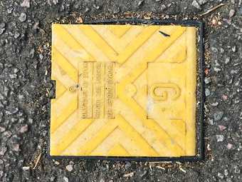 Square yellow electrical or gas plastic flap on the road surrounded by tarmac