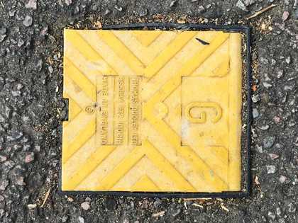 Square yellow electrical or gas plastic flap on the road surrounded by tarmac