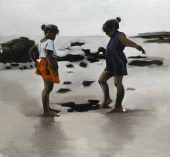 two young girls play on sand by the sea
