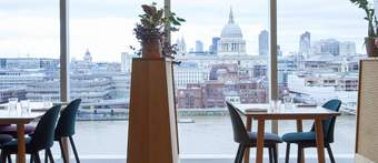 Restaurant tables in front of large glass window looking over River Thames and St Paul's Cathedral
