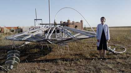 Vidokle film still of someone standing in a barren field with a large sculpture