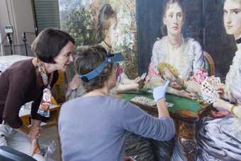 two women inspect and look at a painting