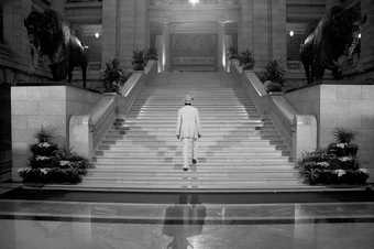 Shezad Dawood film still from A Mystery Play 2010 showing a man dressed in a white suit going up a wide marble staircase