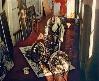 William Green using his bicycle tyres to spread liquid paraffin and black bitumen into the surface of the canvas, 1957