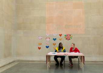 Two artists sit at a table in Tate Britain with cut out hearts in the background