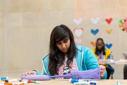 A child sits at a table in Tate Britain and creates an abstract sculpture made from purple fabric