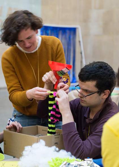 A vistor and artist jointly make a piece of artwork made from colourful stripy socks and paper