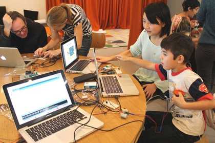 children sit on a table next to a laptop