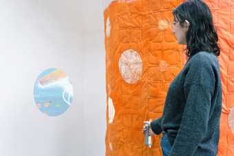 a person stands by an orange quilted wall and a circular projection
