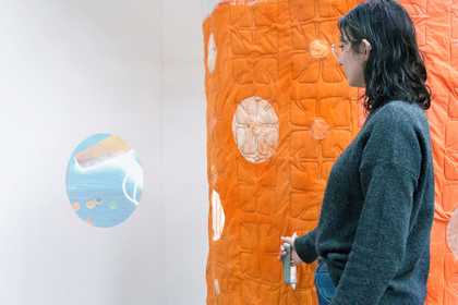a person stands by an orange quilted wall and a circular projection