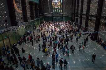 People stand and dance in the Turbine Hall which has been lit with disco balls and lights