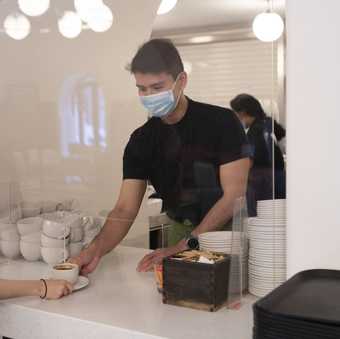 a cafe staff member passes a cup of coffee to a person 