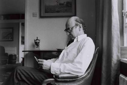 Black and white portrait photograph of Darcy Lange sitting in a chair in a living room