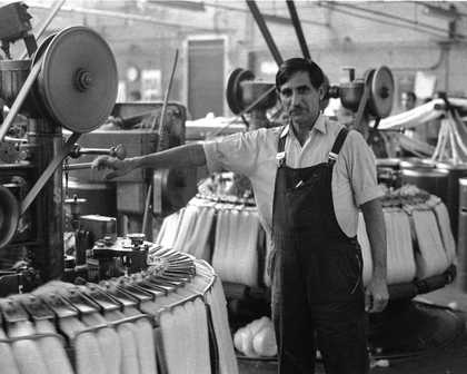 Black and white photograph of Darcy Lange standing in front of industrial machinary