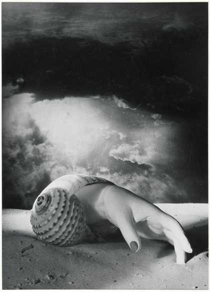 A black and white image of a human hand with painted fingernails emerging from a conch shell. The shell is on a sandy ground and against a cloudy background.