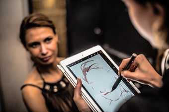 A woman having a digital portrait drawn on a tablet