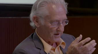 film still of ed ruscha sitting down in a suit and talking in front of a live audience