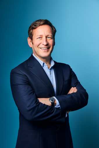 Photographic portrait of Ed Vaizey standing smiling arms crossed