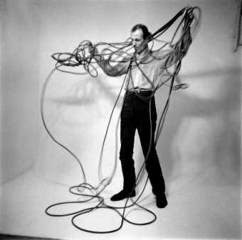 man stood with arms outstretched holding a mass of knotted wires.