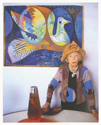 Eileen Agar wearing her Glove Hat 1936 and standing by her painting The Bird’s Nest 1969 at her home in London, 1989