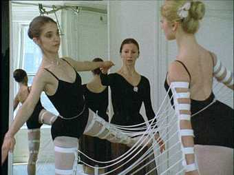 Two ballet dancers raise one leg whilst wearing a series of bands around the legs and arms