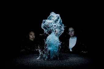 two people look at a water based fountain sculpture in a darkened room