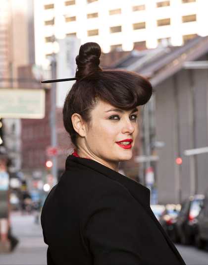 portrait photograph of a figure looking back over the right shoulder to camera. Wearing red lipstick and with hair tied up on the top of the head.
