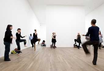 A group of dancers stand on one leg in a white room of a Tate Modern gallery