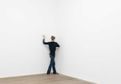 Female dancer is show moving with back turned in the corner of a gallery space