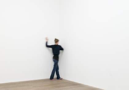 Female dancer is show moving with back turned in the corner of a gallery space