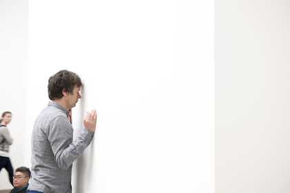 A male dancer leans with his head against a gallery wall, side profile
