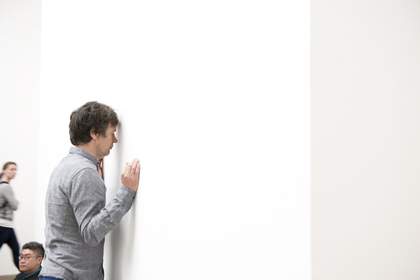 A male dancer leans with his head against a gallery wall, side profile
