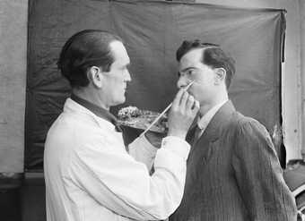 Captain Francis Derwent Wood RA of the Royal Army Medical Corps holds an artist’s palette as he adds the finishing touches to a patient’s new facial plate, photo by Horace Nicholls, c1914–8