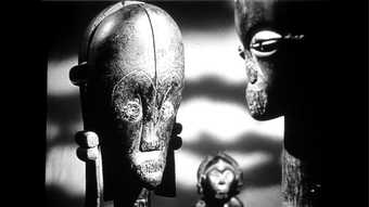 Black and white still of a close up of two statue heads, there is a lot of light and shadow